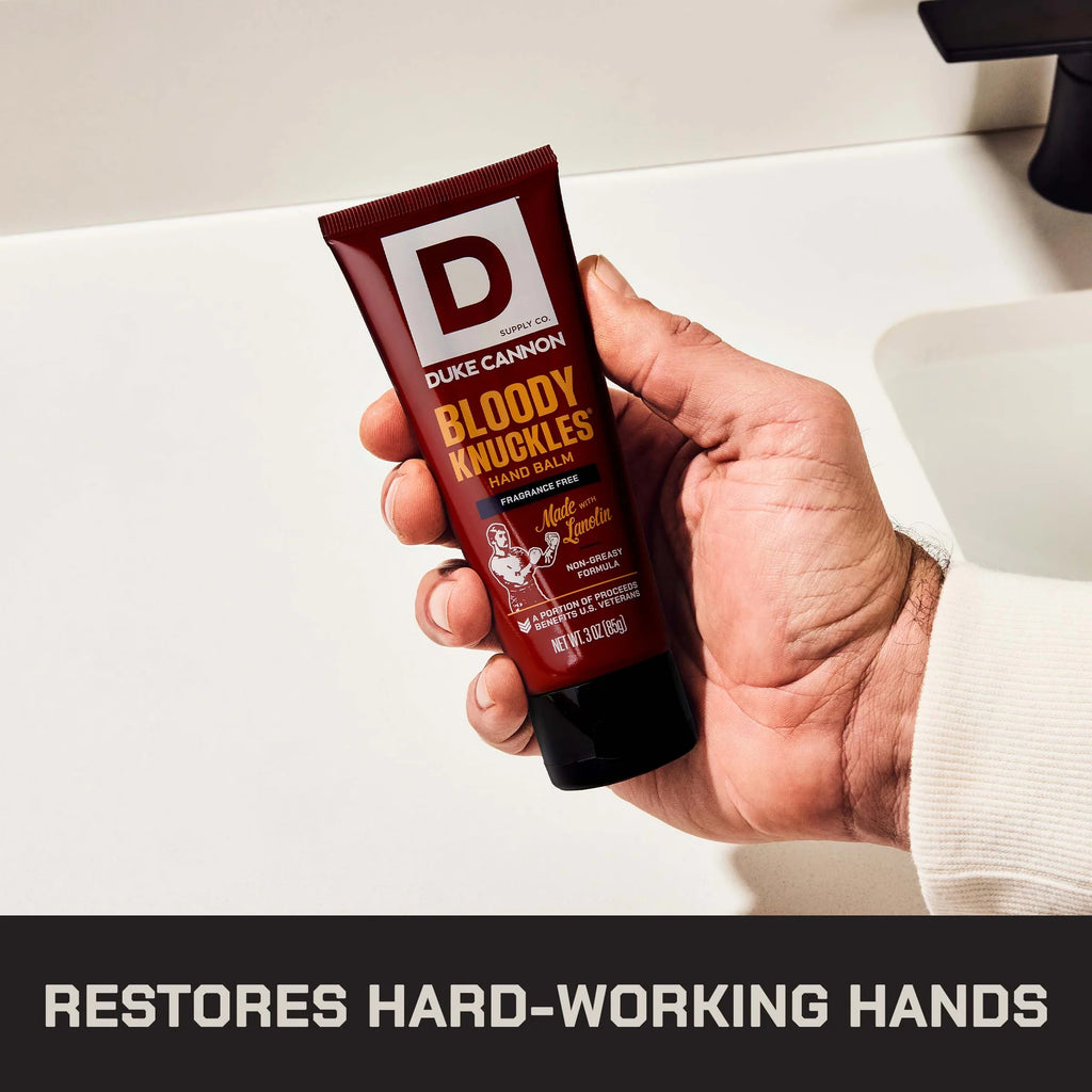 A hand holding a squeeze tube of Duke Cannon Bloody Knuckles Hand Balm