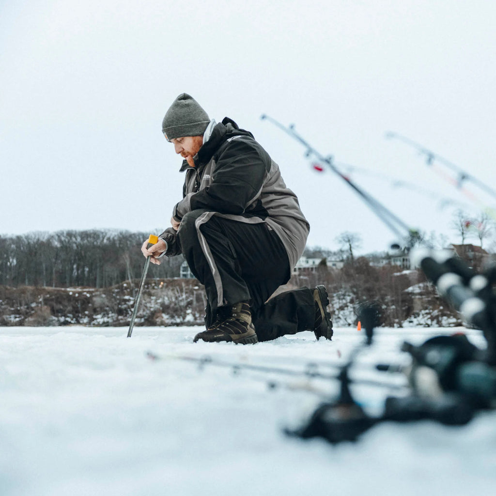 Person wearing LaCrosse Cold Snap II boots while kneeling on a frozen lake with ice-fishing gear