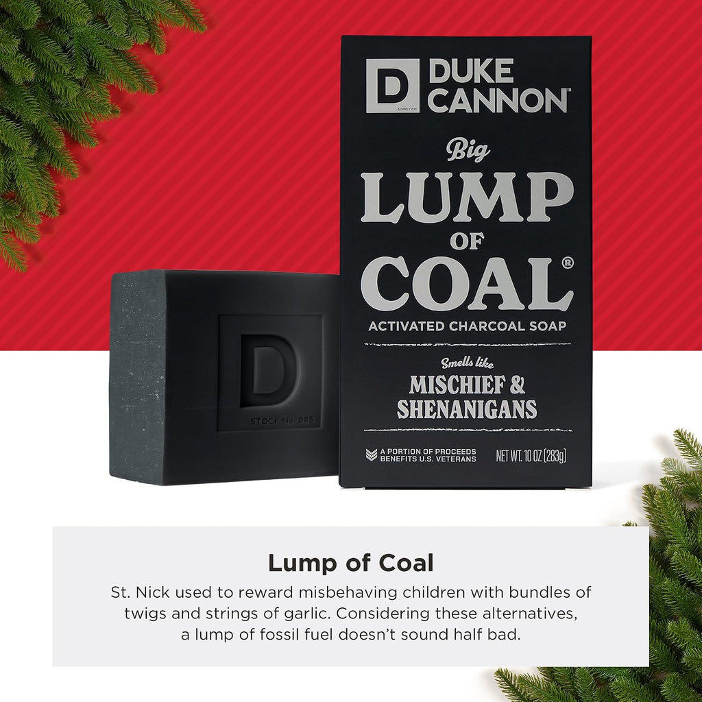 Duke Cannon Big Ass Lump of Coal charcoal soap beside its black box in a holiday display with pine branches